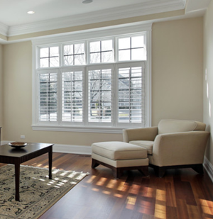 Shutters installed over a large set of four tall windows in a living room with white walls and wood floors.