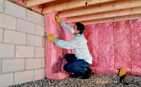 Pink batt fiberglass insulation being installed along the walls of a crawl space.