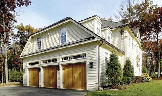 Large white home with three woodgrain garage doors on the side.