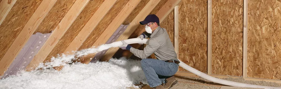 Technician blowing loose-fill insulation into an unfinished attic.